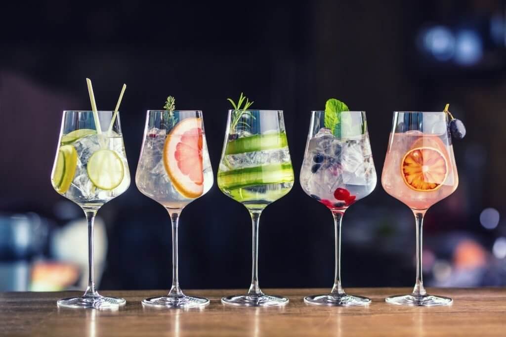 Five glasses of gin, each infused with a distinct fruit or herb, showcasing a variety of flavors and aromas in the infused gins.