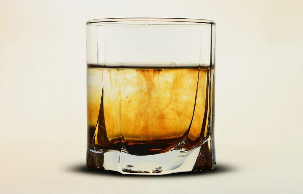 A glass of infused rum, displaying a gradient effect with a rich brown color at the bottom and a clear color on top, indicating the infusion of flavors and colors in the rum.
